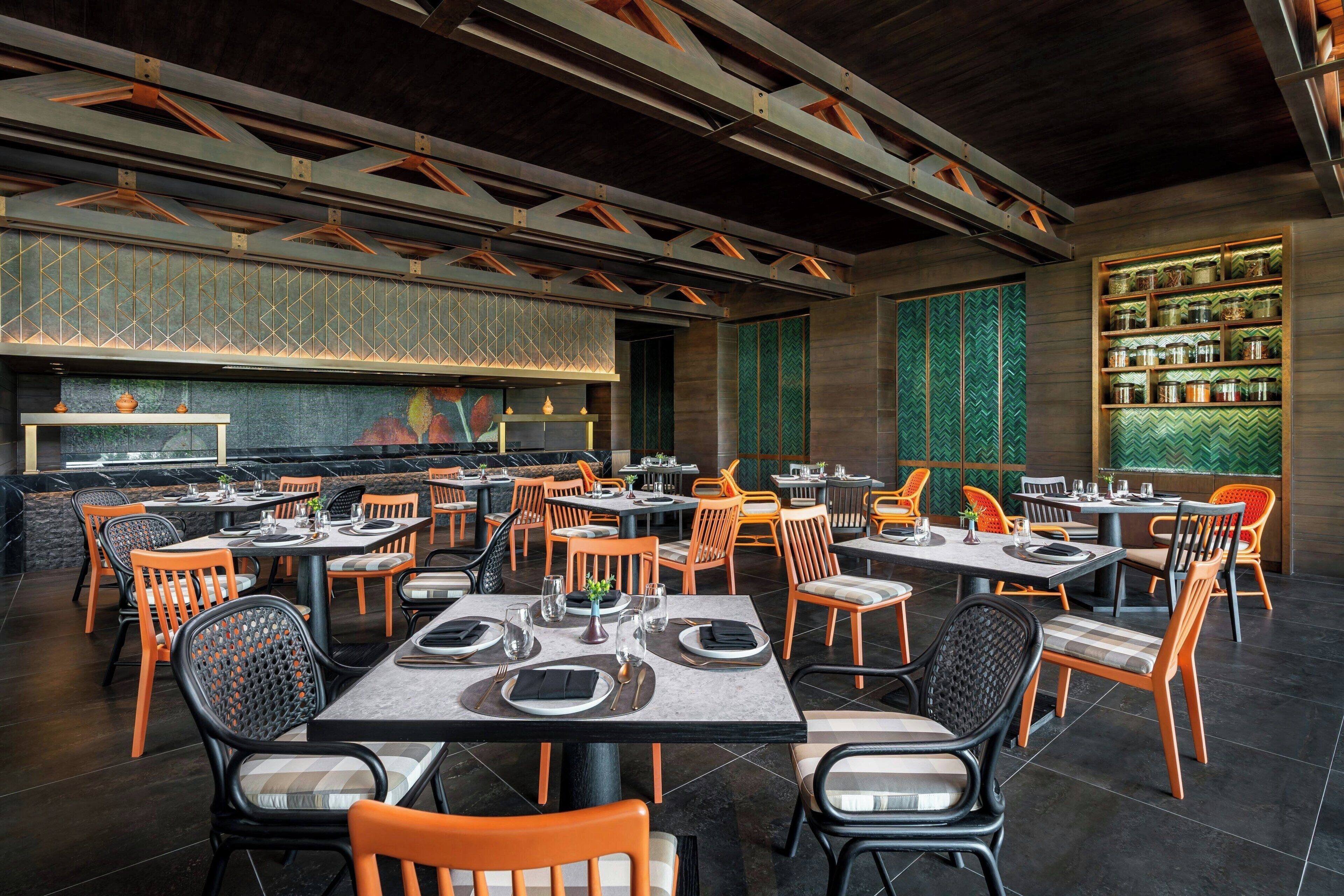 A restaurant with multiple tables and chairs, a patterned wall, and a shelf with jars.