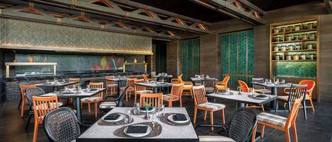 A restaurant with multiple tables and chairs, a patterned wall, and a shelf with jars.