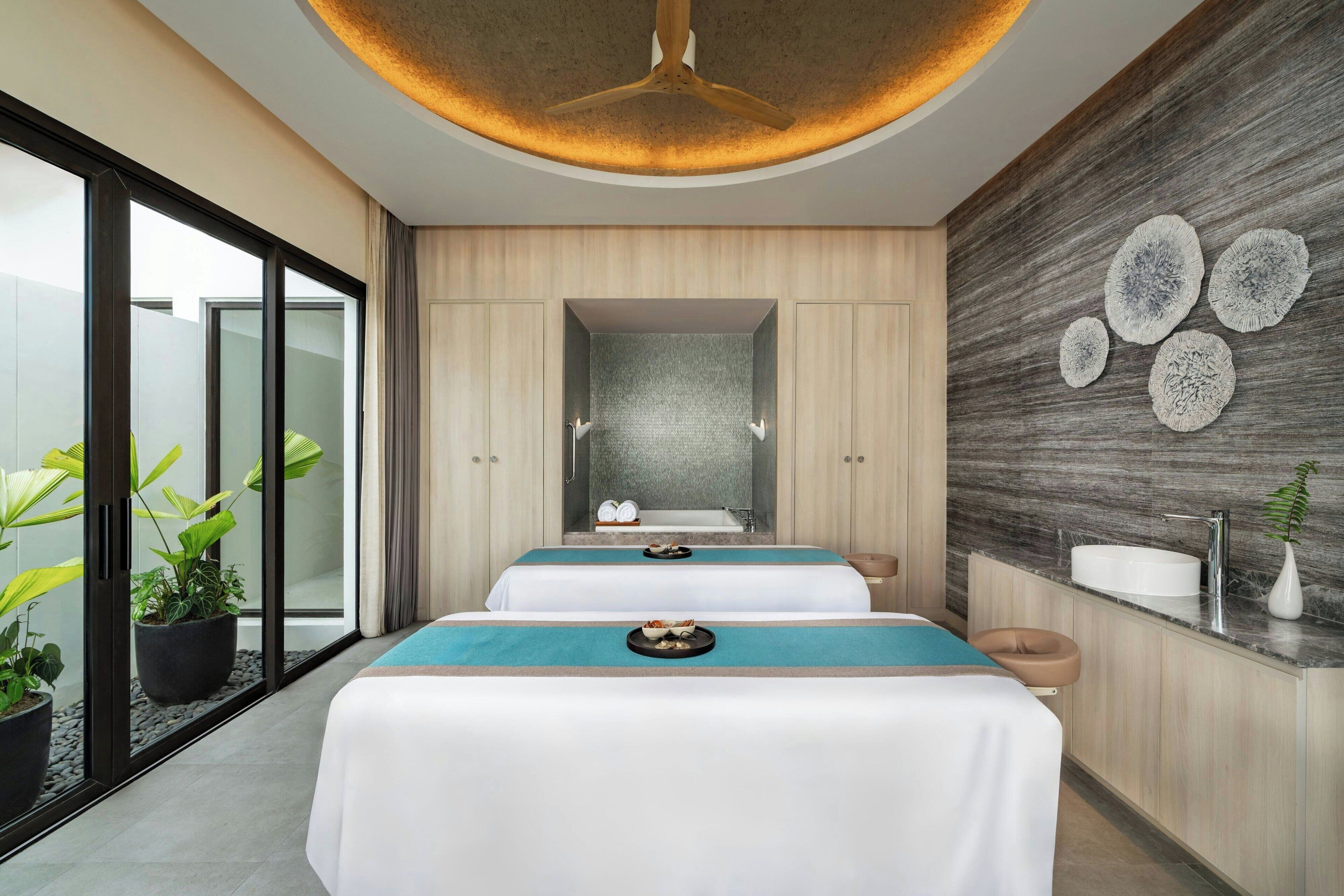 Un moderno spa con un espejo grande, dos camillas de masaje, un lavabo y decoración mural.