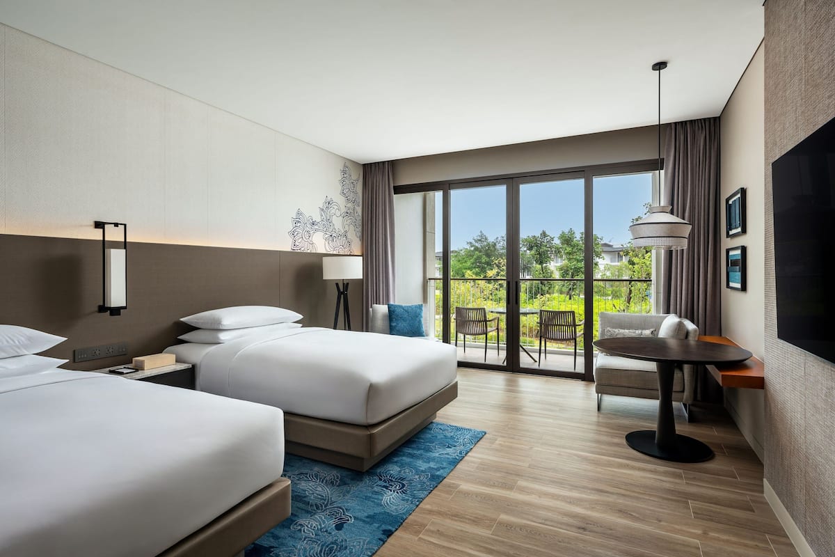 Una habitación de hotel moderna con dos camas, una mesa de comedor y un balcón con mobiliario exterior.