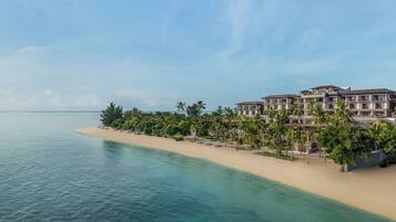 A beachfront hotel with multiple buildings, a sandy beach, and palm trees.