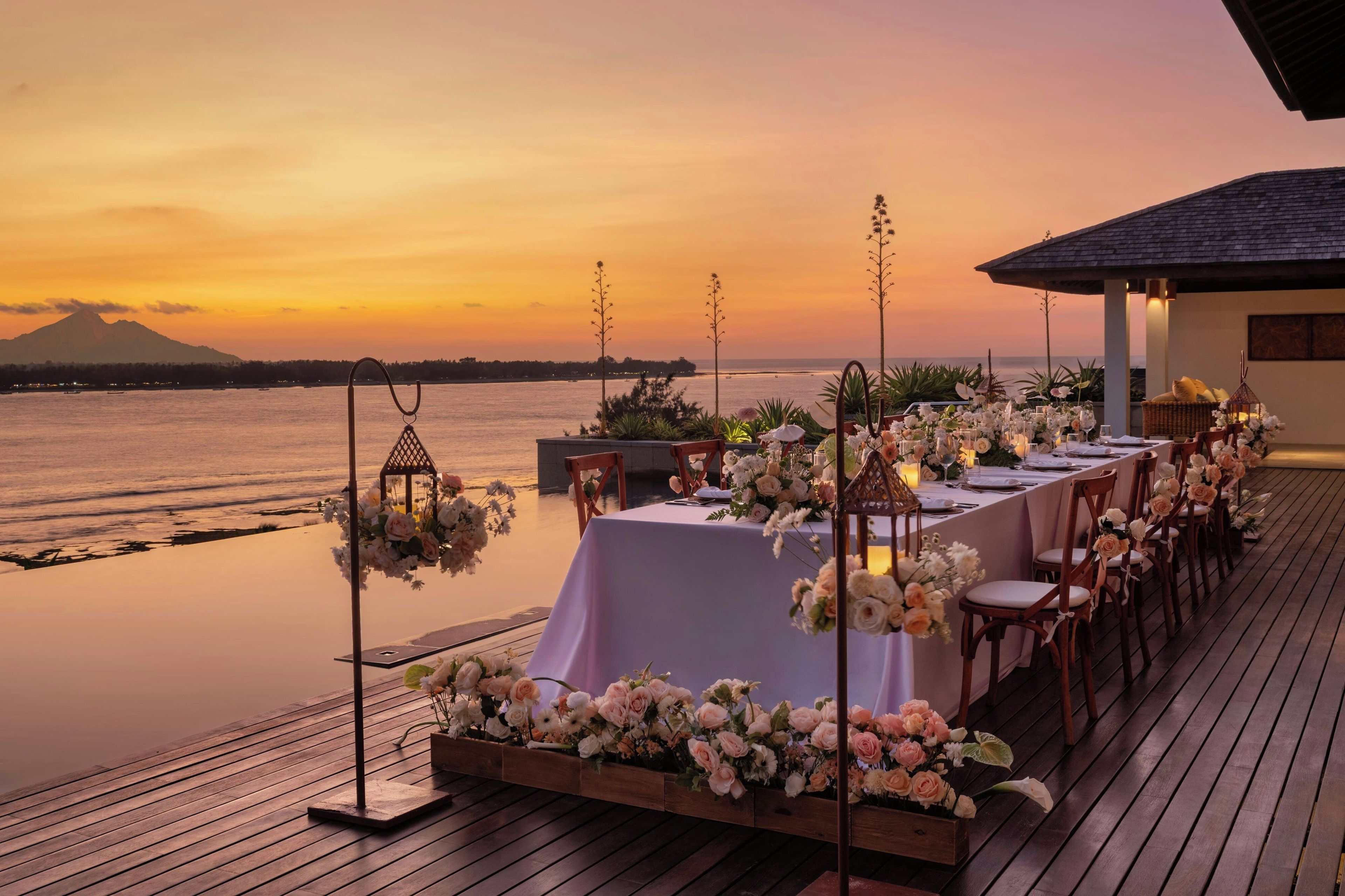 An outdoor dining area with a view of a mountain and the sea at sunset.