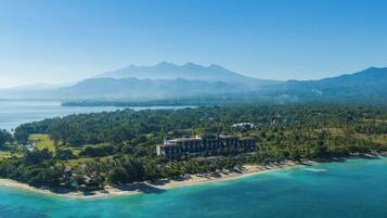 A coastal resort with a beachfront, lush greenery, and a mountain backdrop.