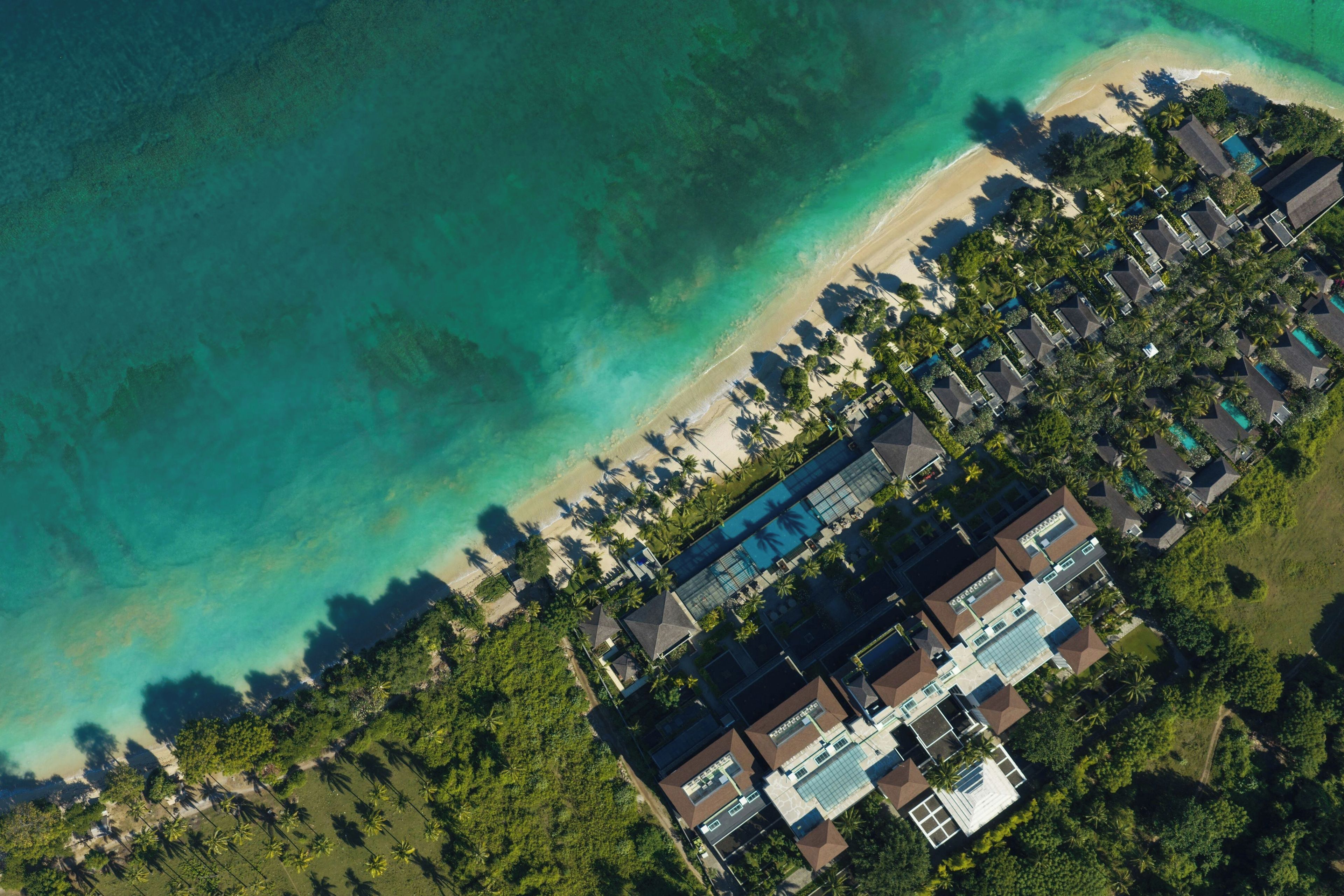 An aerial view of a resort with a beach, pool, and dense tropical vegetation.