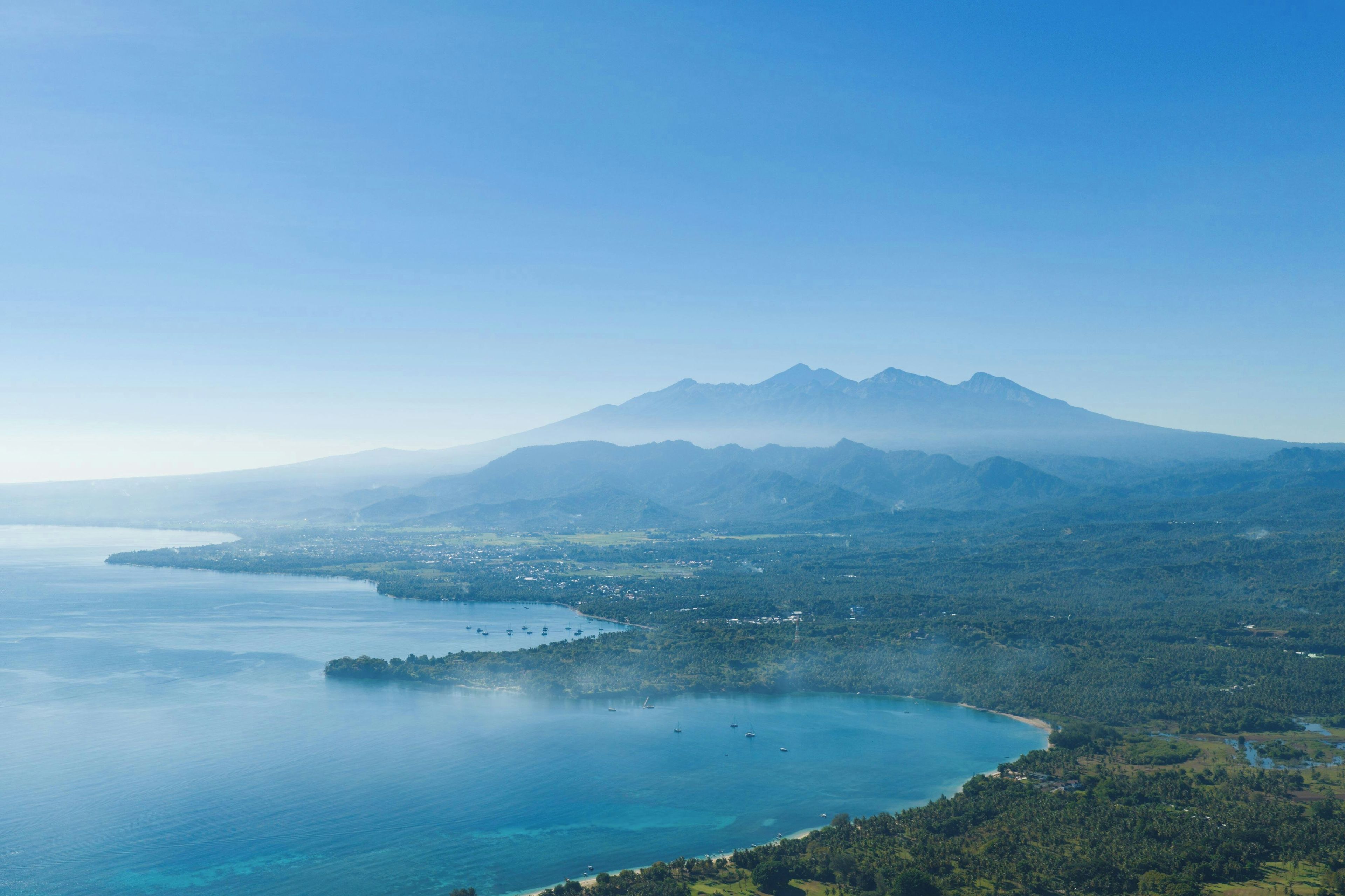 A coastal landscape with a mountain range, clear skies, and a calm sea.