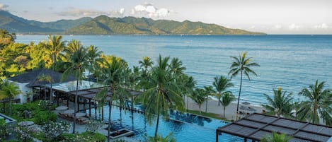 A resort with a swimming pool, lounge chairs, and palm trees.