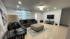 A modern living room with a sofa, ottoman, and a glass coffee table. - Family Getaway - Private Pool - Sleeps 8 (New Port Richey)
