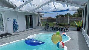 A swimming pool with inflatable toys, a covered patio area with chairs, and a view of the backyard. - Family Getaway - Private Pool - Sleeps 8 (New Port Richey)