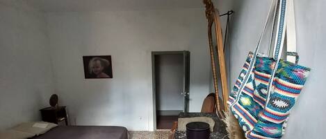 Una habitación pequeña y sencilla con cama, una silla, un escritorio y un bolso colgado.