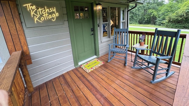 A porch with a green door, two rocking chairs, and a small table with a potted plant. - Welcome to The Kitschy Kottage (Rogersville)