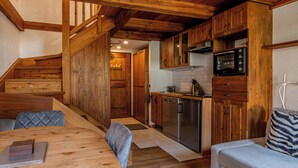 Een houten interieur met een eettafel, stoelen, een bank, een keuken met apparatuur en een trap.