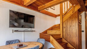 Een houten trap met een tv aan de muur boven een eethoek.
