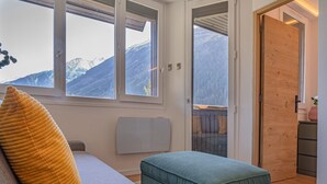 A room with a sofa, ottoman, and a view of mountains through large windows.