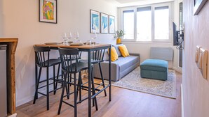 A modern dining area with a wooden table, black chairs, and a grey sofa with yellow cushions.