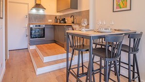 A modern kitchen with a built-in oven, a coffee machine, and a dining area with a table set for four.