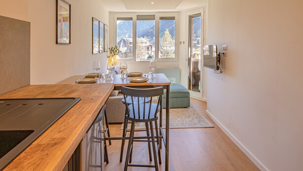 A modern kitchen with a wooden countertop and bar seating, a dining area with a table set for two, and a view of mountains through large windows.