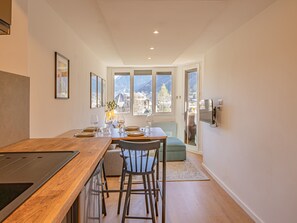 Una cocina moderna con encimera de madera y asientos tipo barra, un comedor con mesa lista para dos personas, y vistas a montañas a través de amplios ventanales.