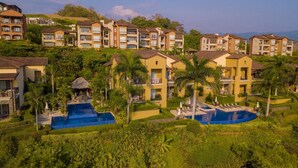 Un resort con varias construcciones de dos pisos, una piscina central y abundante vegetación circundante.