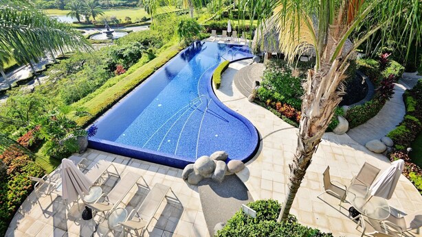 Una piscina de diseño curvo, rodeada de sillas de descanso y un jardín bien cuidado.