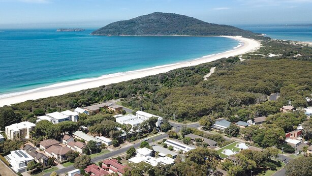 An aerial view of a coastal residential area with houses, a beach, and a mountain in the background. - Opposite Bennetts Beach (Hawks Nest)
