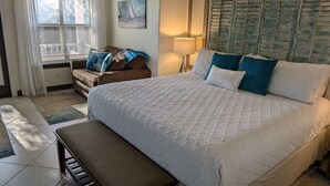 A bedroom with a large bed, a bench, a chair, and a window with curtains. - A Dose of Destin (Destin)