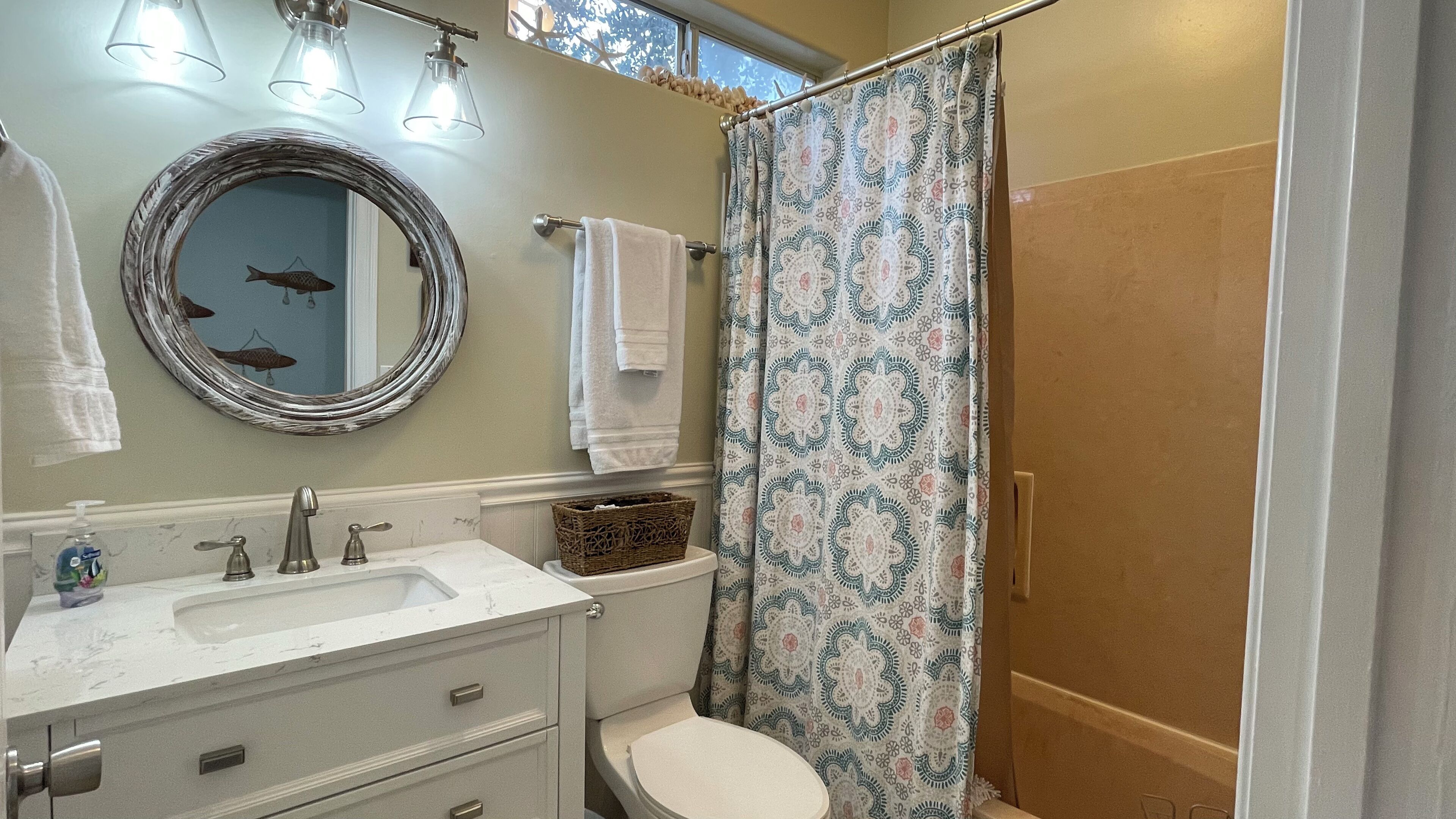 A bathroom with a sink, mirror, and toilet. There is a shower curtain with a pattern.