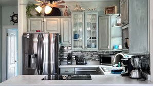 A modern kitchen with stainless steel appliances, a central island, and a stone backsplash. - A Dose of Destin (Destin)