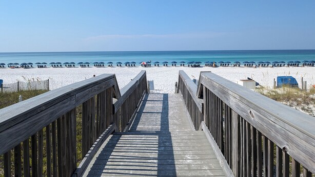 A wooden boardwalk leading to a beach with umbrellas and beach chairs. - A Dose of Destin (Destin)