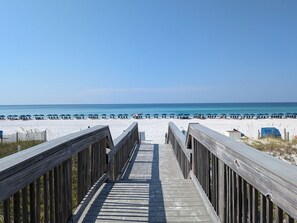 A wooden boardwalk leading to a beach with umbrellas and beach chairs. - A Dose of Destin (Destin)