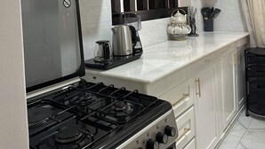 A compact kitchen with white cabinets, a gas stove, a coffee maker, and a window with curtains.