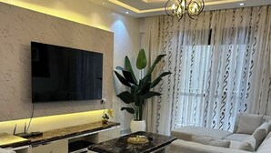 A modern living room with a flat-screen TV, a sofa, a coffee table, and a decorative plant.
