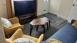 Un salon doté d’un téléviseur à écran plat, de canapés jaunes et bleus, d’une table basse et d’une porte à cadre blanc.
