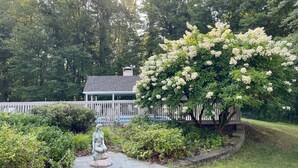 Ein Garten mit einer Statue, einem Gartenpavillon und einem Baum mit weißen Blüten.