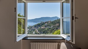 A room with a large window overlooking a coastal landscape with hills and a body of water.