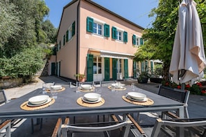 An outdoor dining area with tables set for four, a building with green shutters, and a large umbrella. - VILLA DUFOUR 2 - Luxury, Swimming Pool, and Dream View (Zoagli)