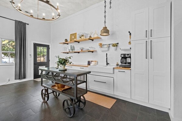 Una cocina moderna con armarios blancos, estantes de madera, un carrito y una lámpara colgante.