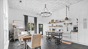 A modern kitchen with white cabinets, a dining area with a wooden table and chairs, and a chandelier.
