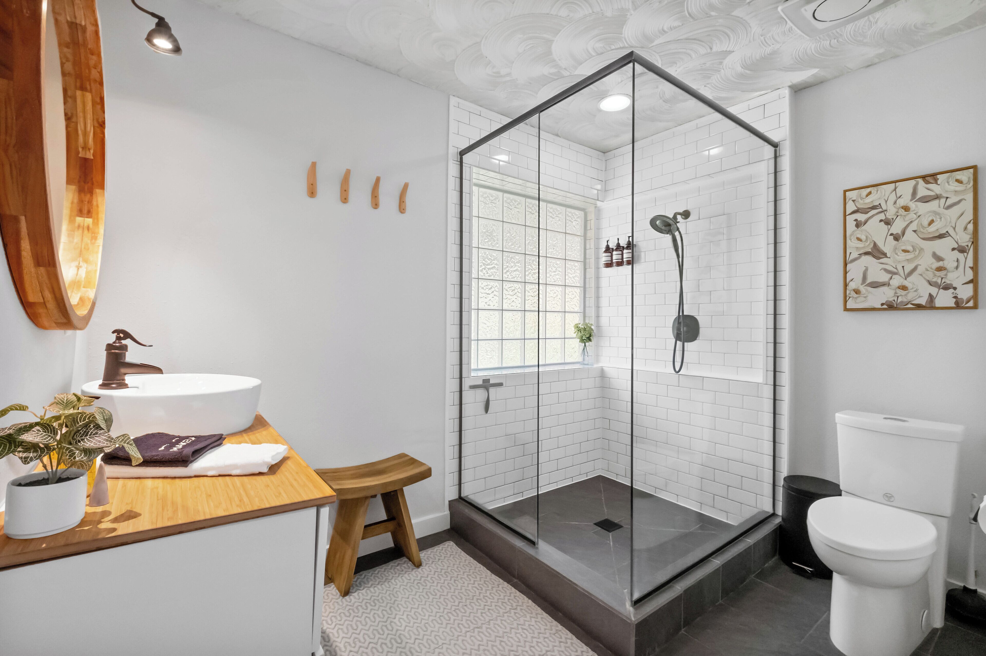 A modern bathroom with a white sink, wooden countertop, and a glass-enclosed shower.