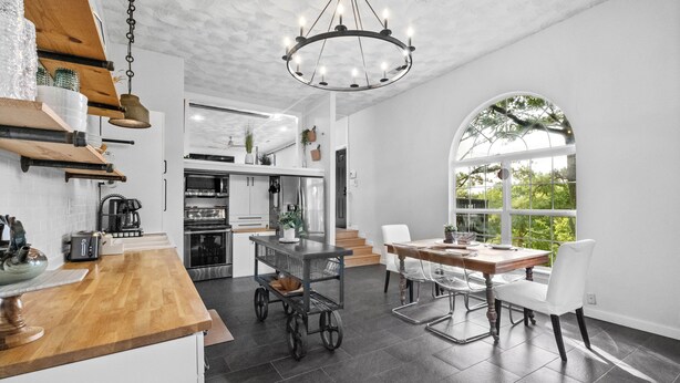 A modern kitchen with a wooden countertop, a chandelier, and a dining area with a table and chairs.