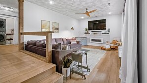 A modern living room with a sofa, coffee table, and a TV. There is a ceiling fan, a plant, and a wooden floor.