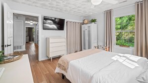 A bedroom with a bed, a TV, a wardrobe, a ceiling fan, and a window with curtains.