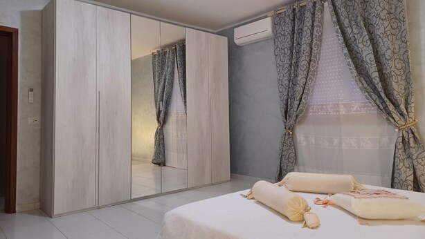 Un dormitorio con un armario grande, una cama con almohadas y un ventanal con cortinas estampadas.