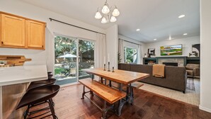 A modern kitchen with wooden cabinets, a dining table with benches, and a large window overlooking a garden. - Mt. Bachelor Retreat! Hot tub, game room, family suite - great for large groups! (Bend)