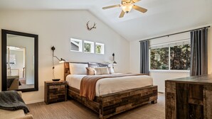 A bedroom with a wooden bed frame, a large mirror, bedside lamps, and a view of the outdoors through a window. - Mt. Bachelor Retreat! Hot tub, game room, family suite - great for large groups! (Bend)