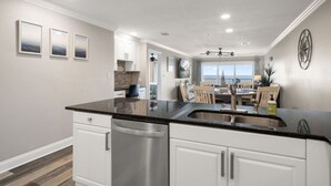 A modern kitchen with a central island, white cabinetry, and a view to the dining area. - Sea Oats Condo #302 Direct Gulf with Heated Pool (Redington Shores)
