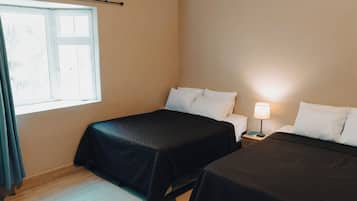 Habitación de hotel con dos camas, una ventana, una mesita de noche con lámpara y una cortina.