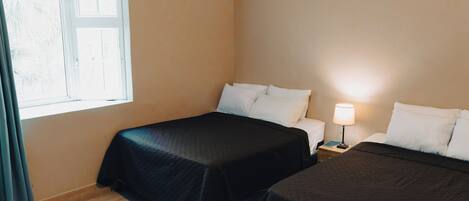 Et hotelværelse med to senge, et vindue, et natbord med en lampe og et gardin.