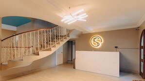 Een modern ingerichte receptie met een gebogen trap, een receptiebalie en een opvallend verlicht logo aan de muur.