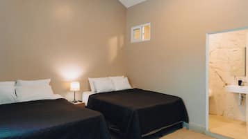A hotel room with two beds, a nightstand with a lamp, a small window, and a bathroom with a marble wall and sink.