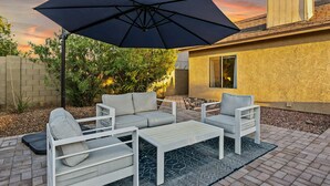 An outdoor patio with a white sofa set, a coffee table, and a large black umbrella. - Cozy and Stylish Home, Convenient Location, Putting Green and Grill  (Chandler)